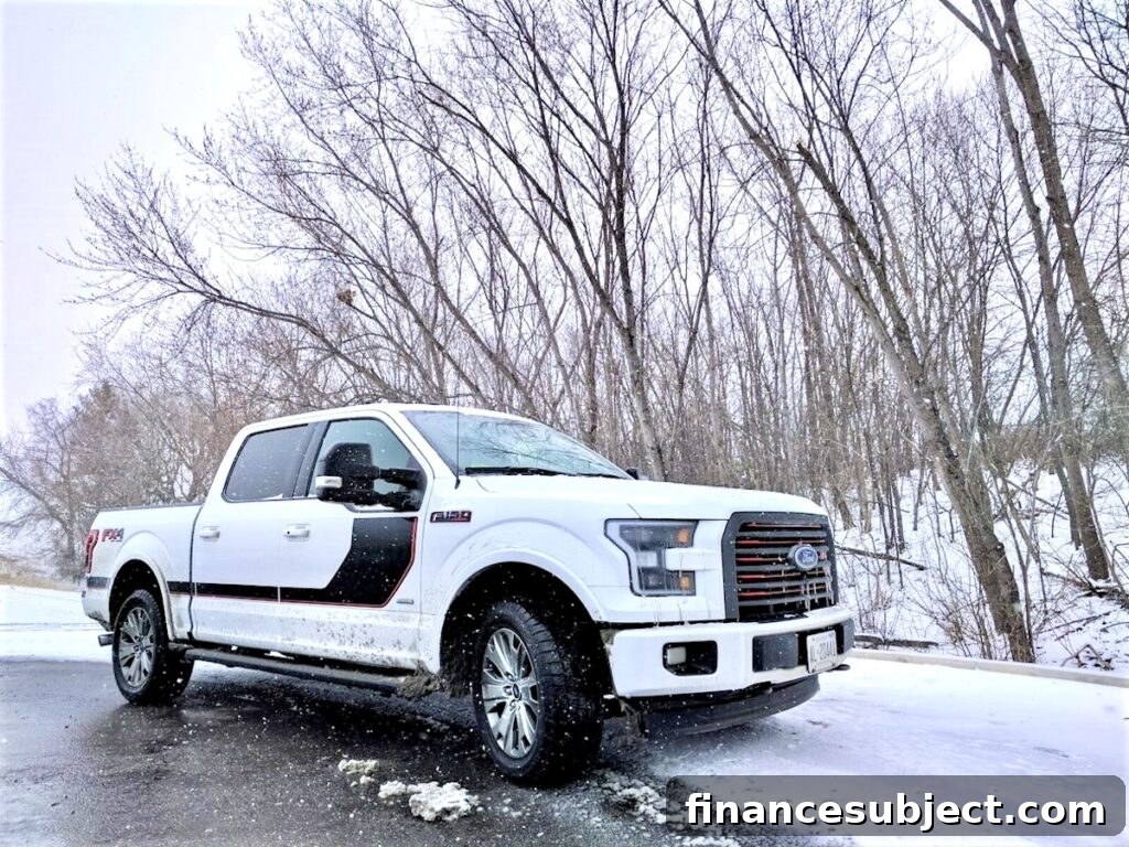 A white Ford F-150 pickup truck drives on a snowy road