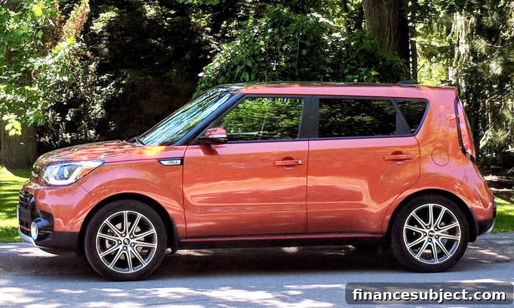 An orange Kia Soul sits on a driveway shaded by trees