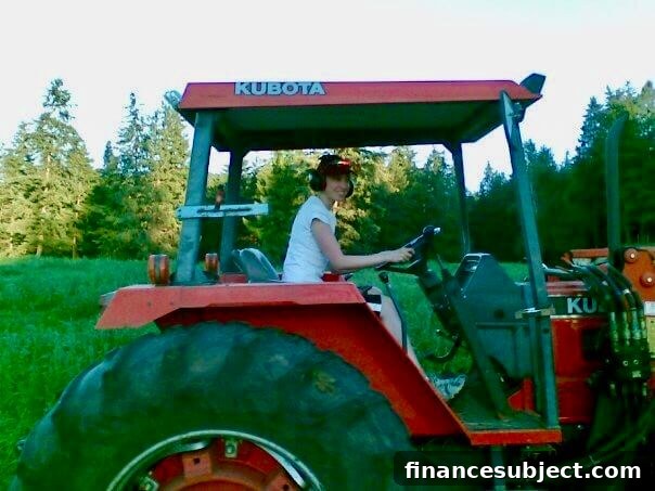 A woman at the wheel of an orange tractor in a forest
